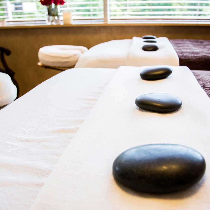 A serene spa treatment room, featuring massage tables adorned with plush towels and massaging stones, creating an inviting atmosphere for relaxation and wellness.