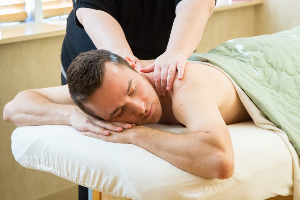 A patient at Bella Via Medical Spa receiving a neck massage while lying down with closed eyes.