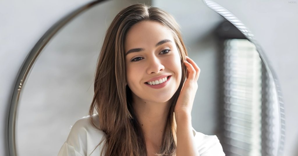 Young woman smiling in front of a mirror (model)